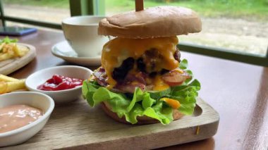 Marul ve sebzeli büyük, sulu bir burger. Yanında patates kızartması ve sosla birlikte bir kafede, ahşap tepside servis ediliyor.