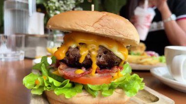 Marul ve sebzeli büyük, sulu bir burger. Yanında patates kızartması ve sosla birlikte bir kafede, ahşap tepside servis ediliyor.