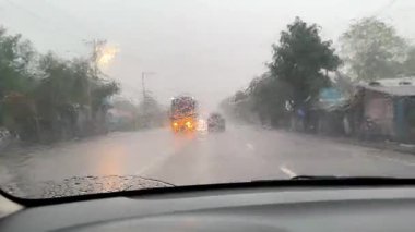 Araba fırtınada yolda gidiyor, ön cam silecekleri şiddetli yağmurdan camı temizliyor, arabanın içini görüyor..