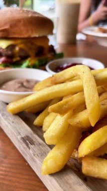 Kafedeki ahşap tepside soslu büyük sulu hamburger ve patates kızartması.. 