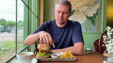 Kafede bir adam soslu patates kızartması ve hamburger yiyor..