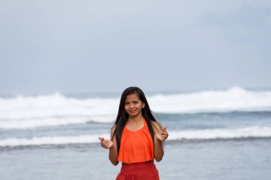 Gülümseyen genç, güzel Asyalı kadın deniz kenarında parmaklarıyla kalp işareti yapıyor..