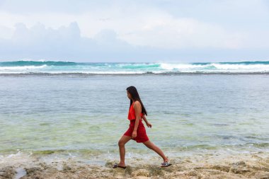 Kendinden emin genç Asyalı kadın sahilde büyük deniz dalgalarının yanında yürüyor..