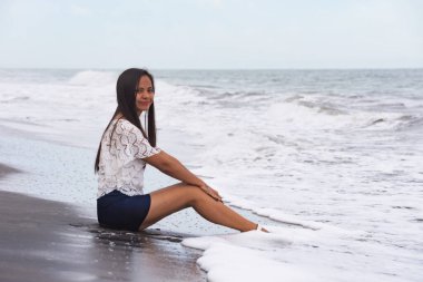 Dalgaların yanındaki kumsalda oturan genç bir kadın..