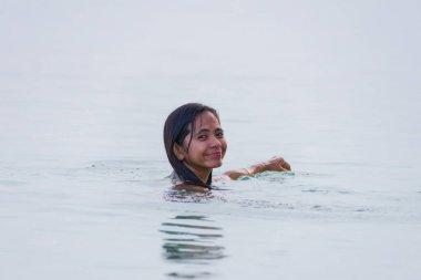 Genç Asyalı kadın denizin sığ sularında yüzmekten ve gülümsemekten hoşlanıyor..