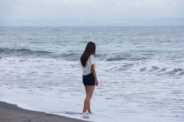 Sahilde dalgaların yanında duran kendine güvenen bir kadın..