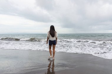 Deniz dalgalarının yanında sahilde yalnız yürüyen kendinden emin genç bir kadın..