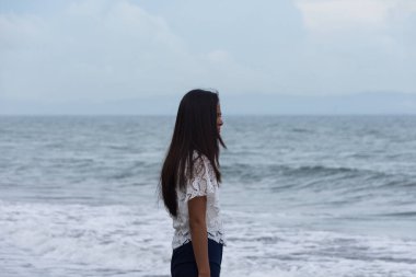 Sahilde dalgaların yanında duran kendine güvenen bir kadın..