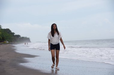 Deniz dalgalarının yanında sahilde yalnız yürüyen kendinden emin genç bir kadın..