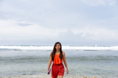 Kendinden emin genç Asyalı kadın sahilde büyük deniz dalgalarının yanında yürüyor..