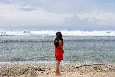 Genç ve yalnız bir kadın fırtınalı bir denizin kıyısında duruyor ve dalgalara bakıyor..