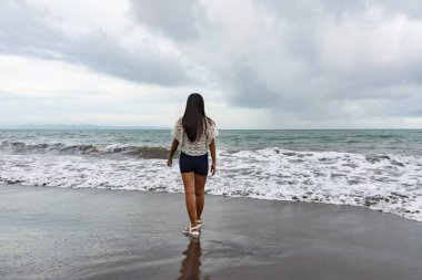 Genç kadın deniz dalgalarının yanında sahilde tek başına yürüyor..