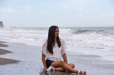 Sahilde oturan mutlu kadın, arkasında dalgalar var..