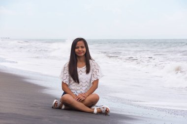 Dalgaların yanındaki kumsalda oturan genç bir kadın..