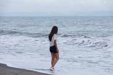 Genç kadın deniz dalgalarının yanında sahilde tek başına yürüyor..