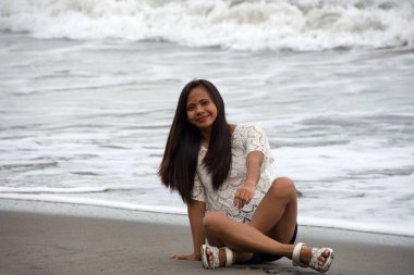 Genç Asyalı kadın gülümsüyor Tropikal dalgalı denizin kıyısında oturuyor.