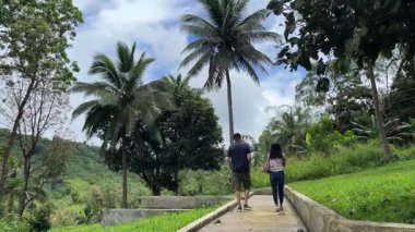Erkek ve kadın, arka planda dağ manzarası olan tropikal ormanda yol boyunca yürüyorlar..