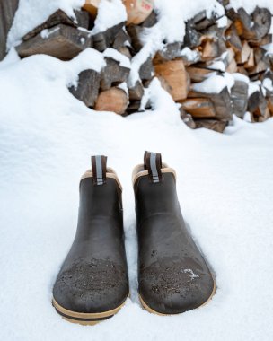 Taze kış karında çizmeler ve odun yığını