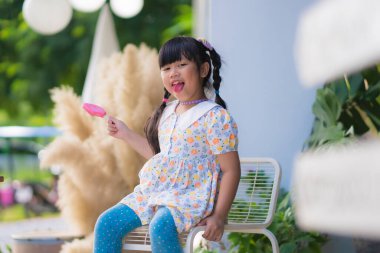Cute smiling little girl eating an ice cream on a stick.