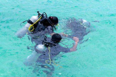 divers in black scuba diving suits with oxygen bottles sink under the sea, Scuba dive training in the sea with a instructor teaching students