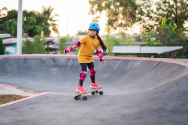 Child or kid girl playing surfskate or skateboard in skating rink or sports park at parking to wearing safety helmet elbow pads wrist and knee support