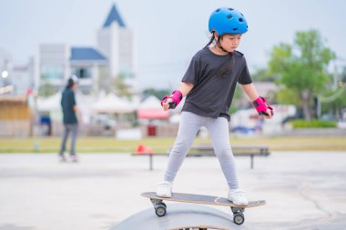 Child or kid girl playing surfskate or skateboard in skating rink or sports park at parking to wearing safety helmet elbow pads wrist and knee support