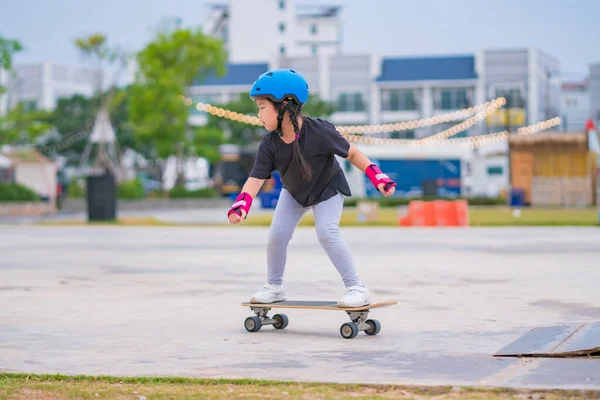 stock image Child or kid girl playing surfskate or skateboard in skating rink or sports park at parking to wearing safety helmet elbow pads wrist and knee support