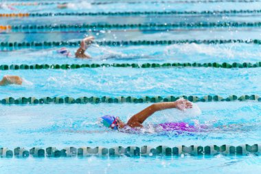 Yüzücü çocuk yüzme havuzunda sırt üstü yüzer. Su sporları ve yarışma, çocuklar için yüzme dersleri..