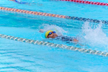 Yüzücü çocuk yüzme havuzunda sırt üstü yüzer. Su sporları ve yarışma, çocuklar için yüzme dersleri..