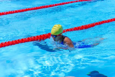 Yüzücü çocuk yüzme havuzunda kurbağalama yüzme stili yüzer. Su sporları ve yarışma, çocuklar için yüzme dersleri.