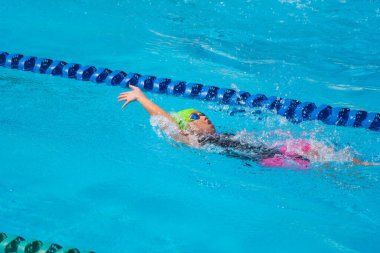 Yüzücü çocuk yüzme havuzunda sırt üstü yüzer. Su sporları ve yarışma, çocuklar için yüzme dersleri..