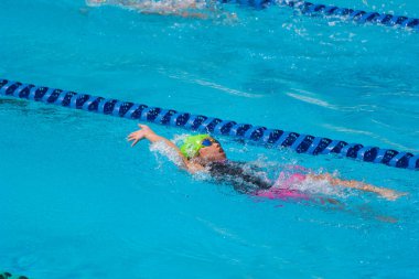 Yüzücü çocuk yüzme havuzunda sırt üstü yüzer. Su sporları ve yarışma, çocuklar için yüzme dersleri..