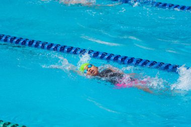 Yüzücü çocuk yüzme havuzunda sırt üstü yüzer. Su sporları ve yarışma, çocuklar için yüzme dersleri..