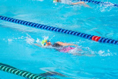 Yüzücü çocuk yüzme havuzunda sırt üstü yüzer. Su sporları ve yarışma, çocuklar için yüzme dersleri..