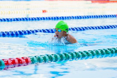 Yüzücü çocuk yüzme havuzunda kurbağalama yüzme stili yüzer. Su sporları ve yarışma, çocuklar için yüzme dersleri.