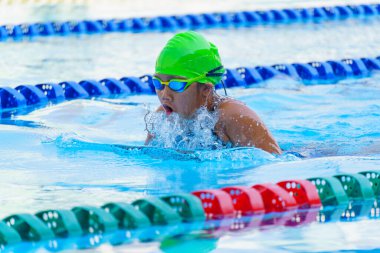 Yüzücü çocuk yüzme havuzunda kurbağalama yüzme stili yüzer. Su sporları ve yarışma, çocuklar için yüzme dersleri.