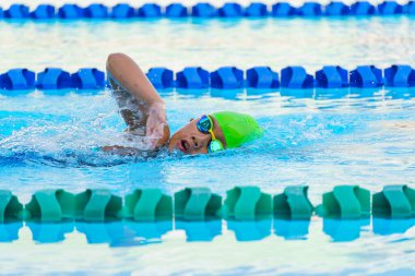 Yüzücü çocuk yüzme havuzunda serbest yüzme stili yüzer. Su sporları ve yarışma, çocuklar için yüzme dersleri..