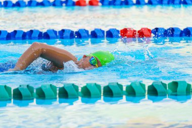 Yüzücü çocuk yüzme havuzunda serbest yüzme stili yüzer. Su sporları ve yarışma, çocuklar için yüzme dersleri..