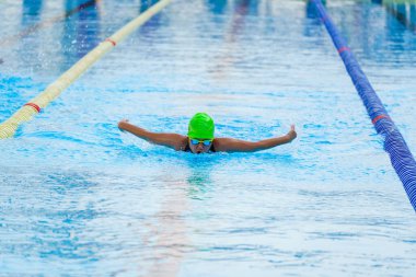 Yüzücü çocuk yüzme havuzunda kelebek yüzme stili yüzer. Su sporları ve yarışma, çocuklar için yüzme dersleri..