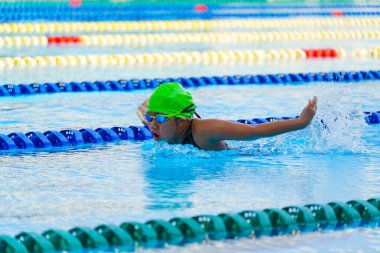 Yüzücü çocuk yüzme havuzunda kelebek yüzme stili yüzer. Su sporları ve yarışma, çocuklar için yüzme dersleri..