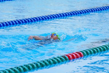 Yüzücü çocuk yüzme havuzunda sırt üstü yüzer. Su sporları ve yarışma, çocuklar için yüzme dersleri..
