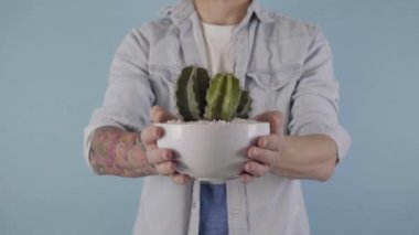 Kameraya yakın bir yerde saksıyı tutan adam. Açık mavi arka planda izole edilmiş. Yüksek kalite 4k görüntü