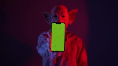 Yeşil ekran akıllı telefon tutan domuz maskeli korkunç bir adam. Cape 'li psikopat, elinde akıllı telefon tutuyordu. Stüdyonun arka planında yeşil ekran vardı. Yüksek kalite 4k görüntü