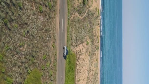 垂直ビデオ海岸近くの道路に沿って車を運転した後 ドローン 砂のビーチで明るい青の参照とクラッシュ波 — ストック動画