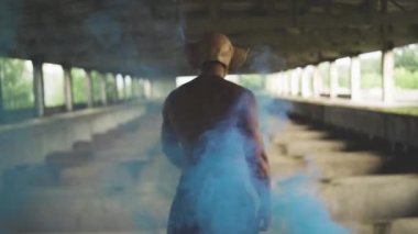 Endüstriyel arka planda maske takan mavi dumanlı kaslı adam. Yüksek kaliteli FullHD görüntüler