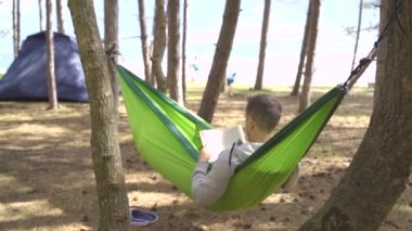 Denizde dinlenirken ağaçların ve çadırların yanında kitap okuyan sakin bir insan. Yüksek kaliteli FullHD görüntüler