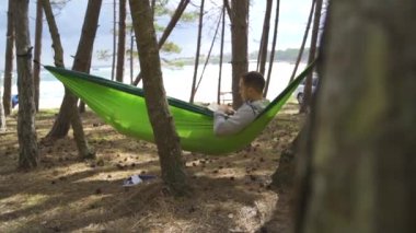 european young man resting outside, reading in summer near trees and tents black sea. High quality FullHD footage