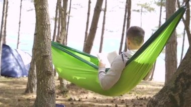 European young man reading outside in the summer near trees and tents near the Black Sea. High quality FullHD footage