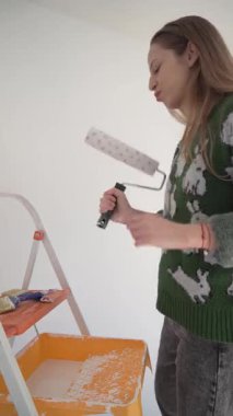 Mutlu genç bir kadın elinde fırça ve silindirle resim yaparken dans eder. DIY ev projeleri, yaratıcılık ve eğlenceli yenilemeler için mükemmel stok görüntüleri.