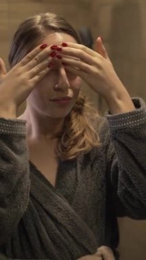 Modern bir banyoda doğal cilt bakım rutini. Bu dikey video, güzellik kampanyaları ve sağlık promosyonları için ideal cilt ürünlerini uygulayan bir kadını çekiyor..